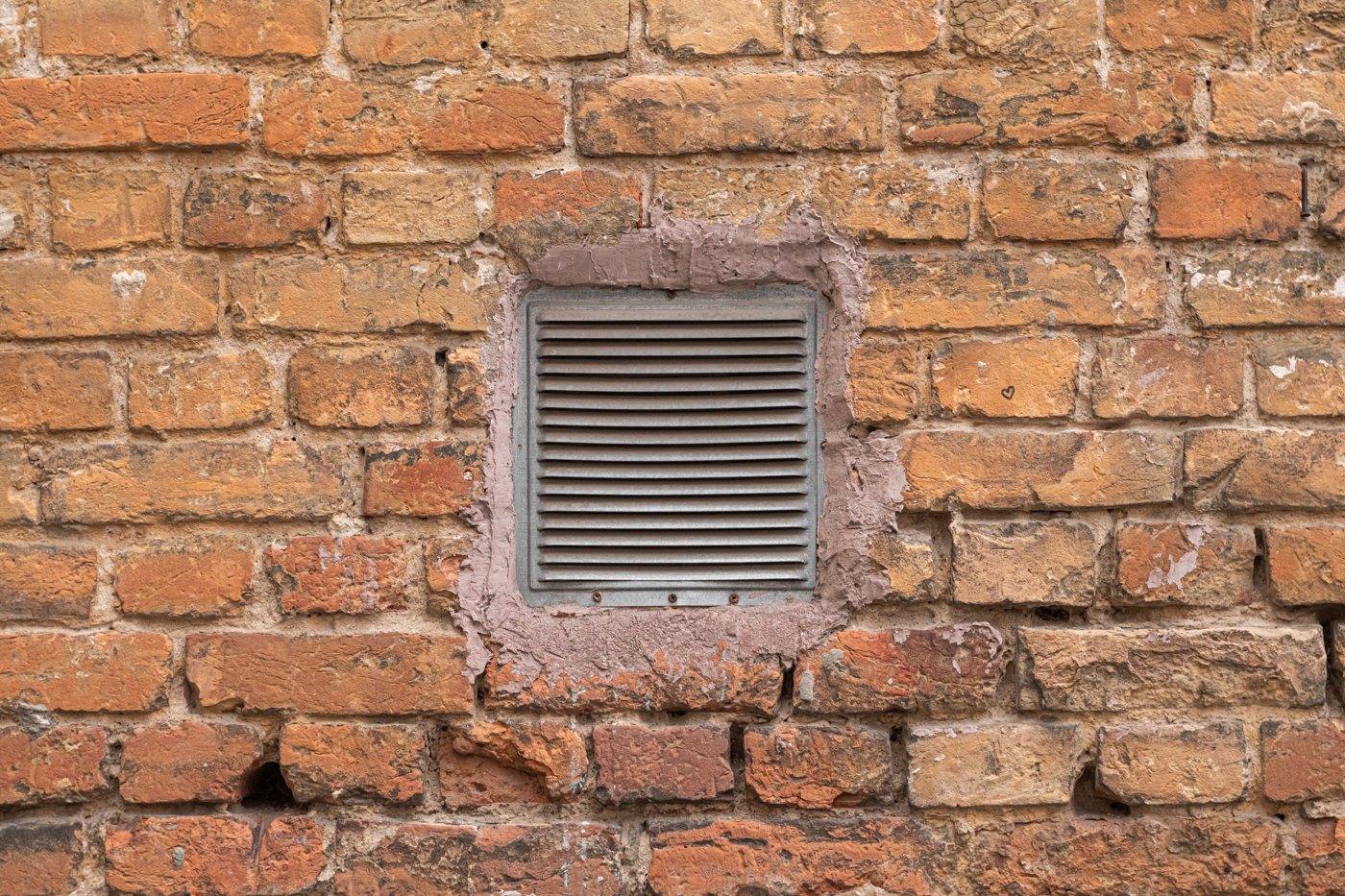 A metal vent grille set into a brick wall