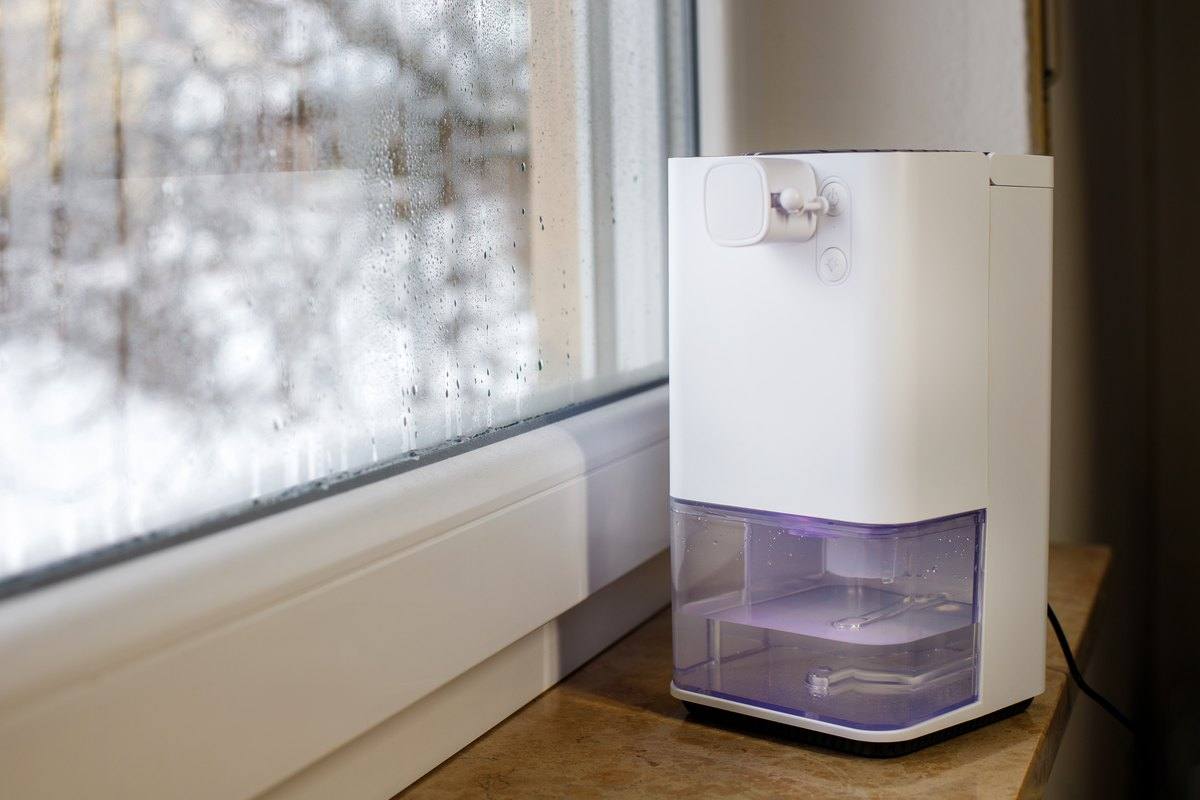 A portable dehumidifier running next to a window covered in condensation