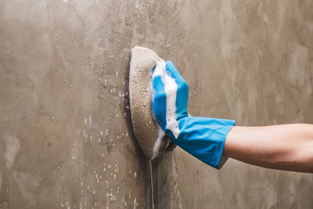 A gloved hand scrubbing a concrete wall with a sponge
